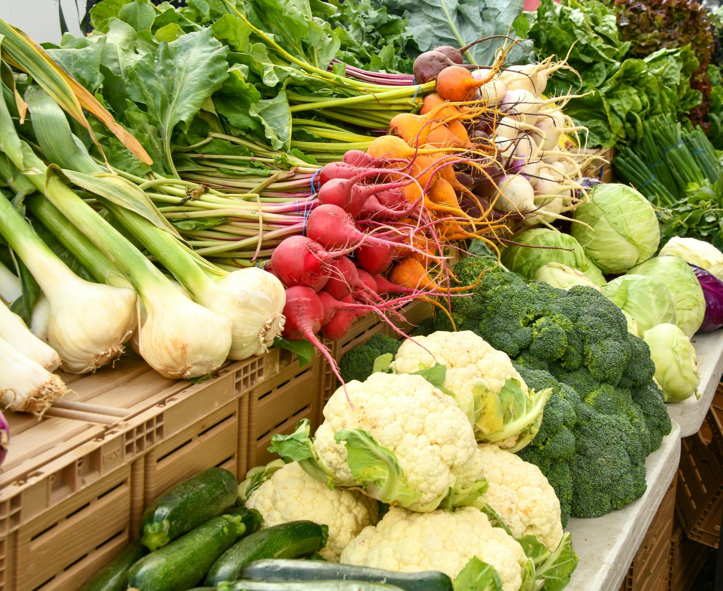 A market stall piled with cauliflower, broccoli, radishes, spring onions and cabbages in crates
