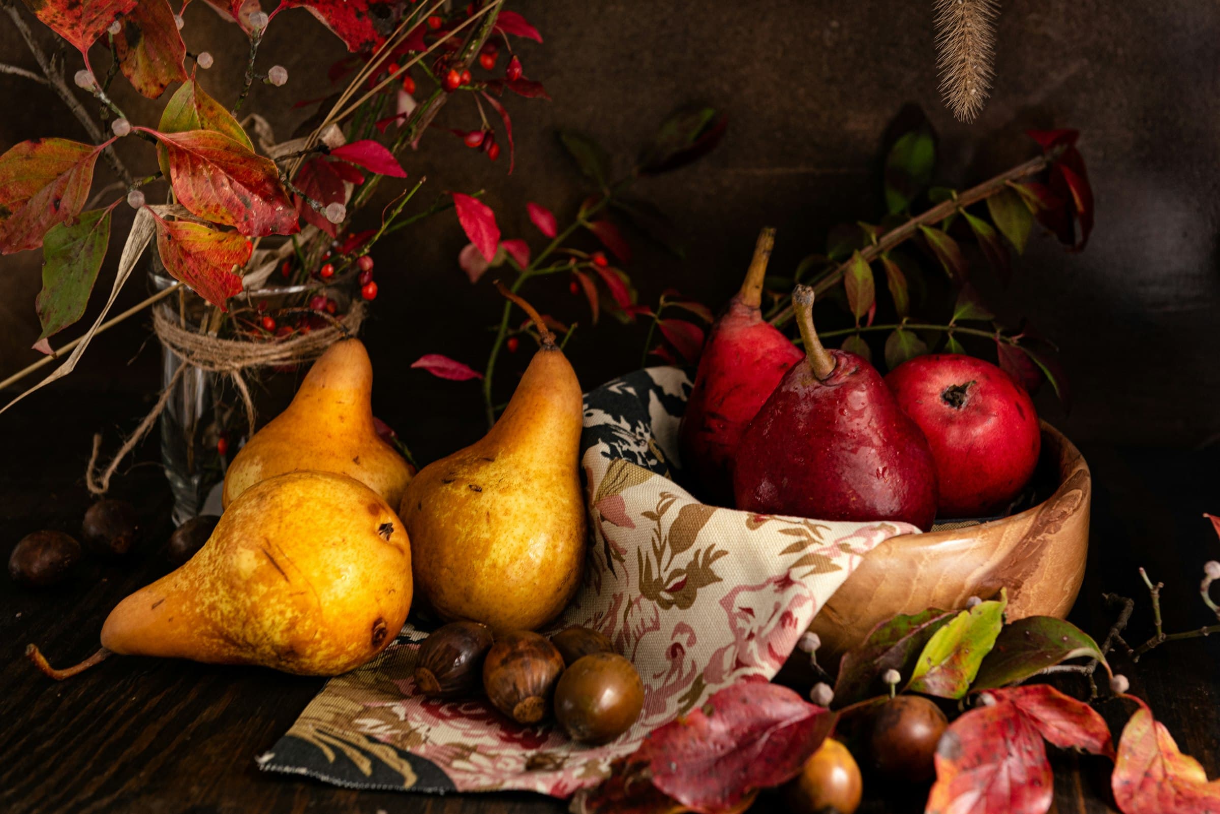 Autumn still life of golden pears, red apples and chestnuts with red leaves on a dark table